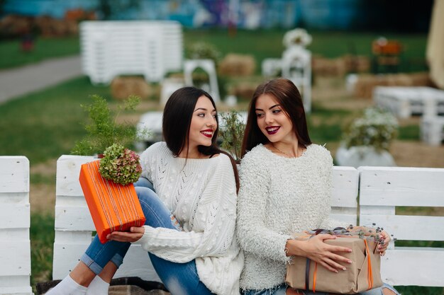 Dos hermosas mujeres sentadas en un banco y sosteniendo en sus manos regalos