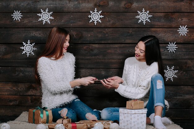 Dos hermosas mujeres sentadas en el suelo con una tableta, entre los regalos de Navidad