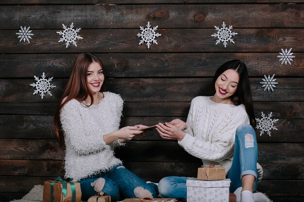 Dos hermosas mujeres sentadas en el suelo con una tableta, entre los regalos de Navidad