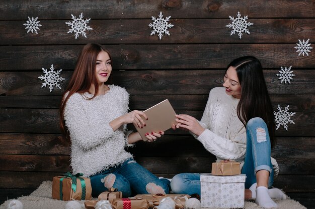 Dos hermosas mujeres sentadas en el suelo con una tableta, entre los regalos de Navidad