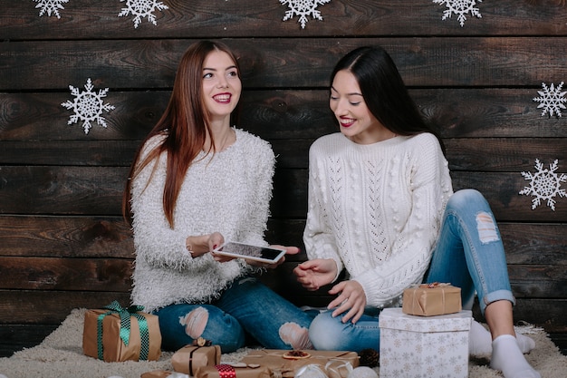 Dos hermosas mujeres sentadas en el suelo con una tableta, entre los regalos de Navidad