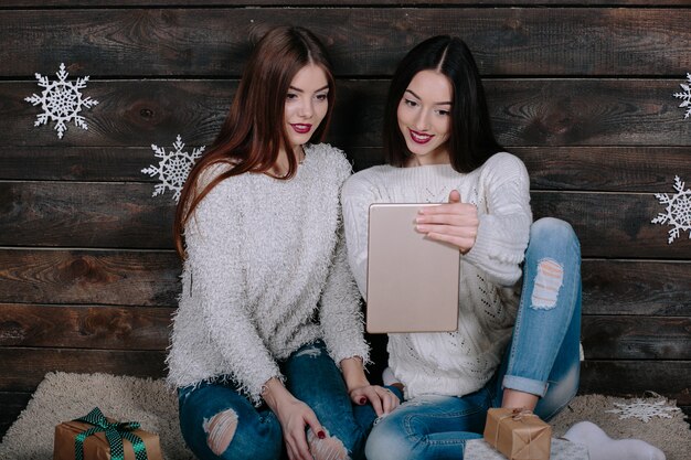 Dos hermosas mujeres sentadas en el suelo con una tableta, entre los regalos de Navidad