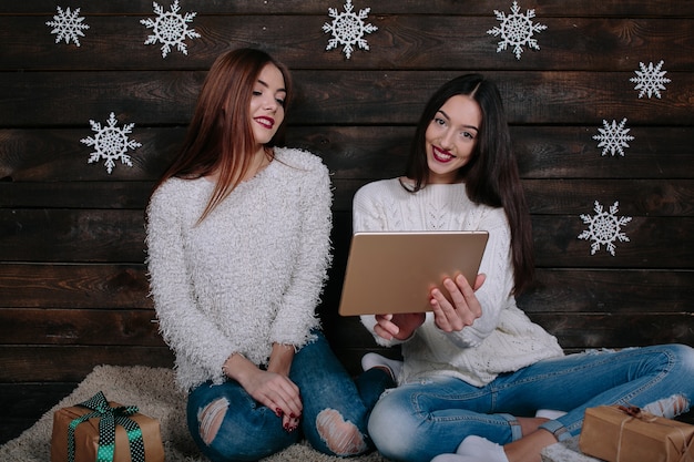 Dos hermosas mujeres sentadas en el suelo con una tableta, entre los regalos de Navidad