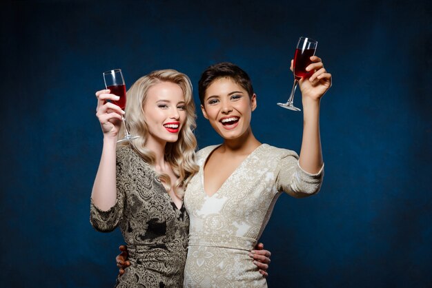 Dos hermosas mujeres en vestidos de noche sonriendo, sosteniendo copas de vino