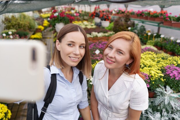 Dos hermosas señoritas haciendo selfie sobre fondo de flores en el invernadero