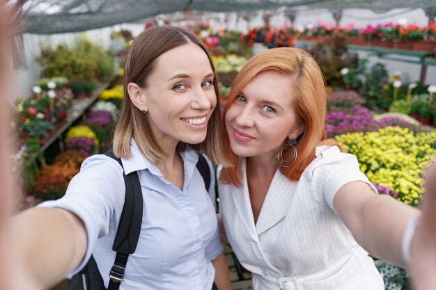 Dos hermosas señoritas haciendo selfie sobre fondo de flores en el invernadero