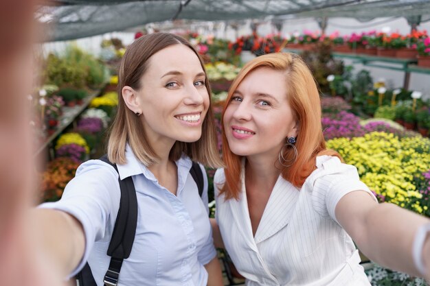 Dos hermosas señoritas haciendo selfie sobre fondo de flores en el invernadero