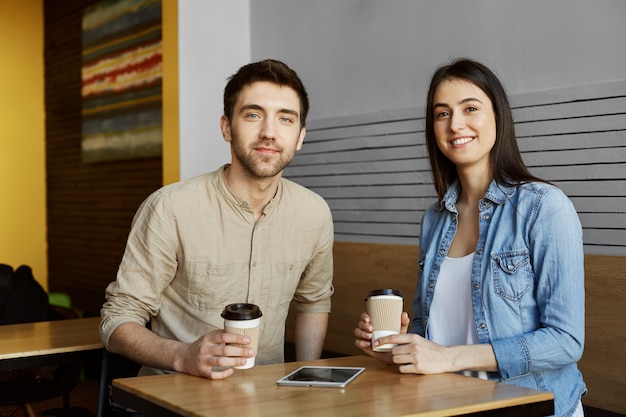 Dos hermosos jóvenes estudiantes sentados en la cafetería, bebiendo cacao, sonriendo, posando para el artículo del periódico universitario