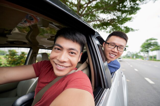 Dos hombres asiáticos viajando en automóvil en la carretera y mirando, y el conductor tomando selfie