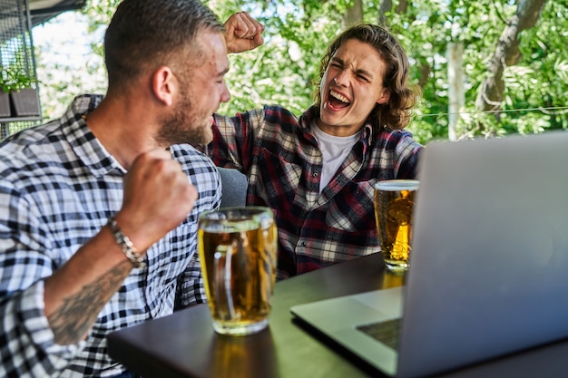 Dos hombres guapos viendo fútbol en un pub y bebiendo cerveza.