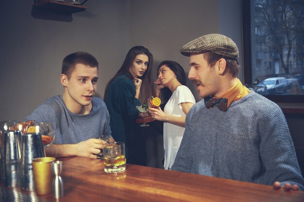 Dos hombres jóvenes en ropa casual hablando mientras está sentado en la barra de bar en el pub