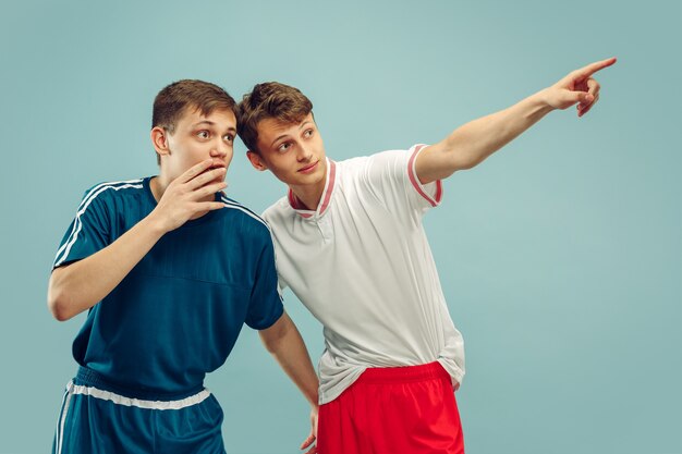 Dos hombres jóvenes en ropa deportiva aislados. Señalando y sorprendido. Retrato de medio cuerpo de hermosos modelos masculinos. Concepto de emociones humanas, expresión facial. Vista frontal.