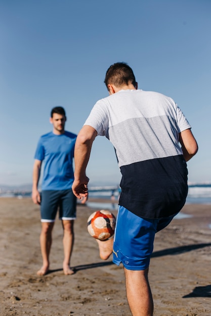 Foto gratuita dos hombres jugando al fútbol en la playa