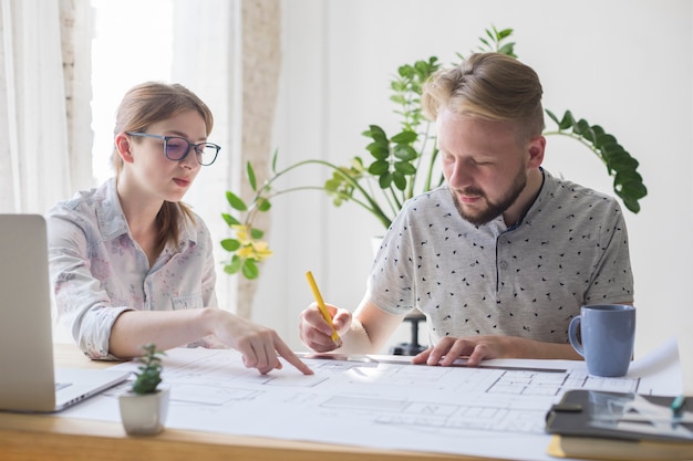 Dos hombres y mujeres arquitecto trabajando en plano en la oficina