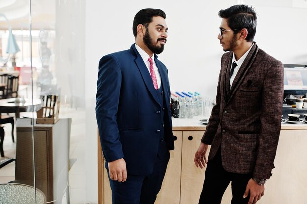 Dos hombres de negocios indios en trajes de pie en el café y discuten entre sí