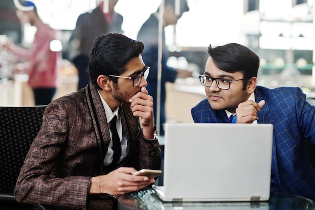 Dos hombres de negocios indios en trajes sentados en la oficina en el café y mirando la computadora portátil