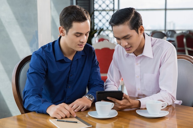 Dos hombres de negocios jovenes que discuten proyecto en Tablet