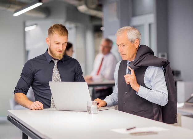 Dos hombres de negocios de pie cerca de la mesa mirando portátil en la oficina