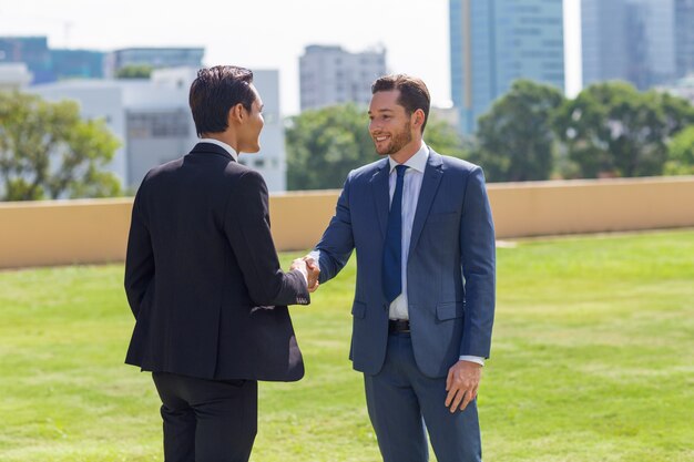 Dos hombres de negocios sonrientes sacudiendo las manos al aire libre