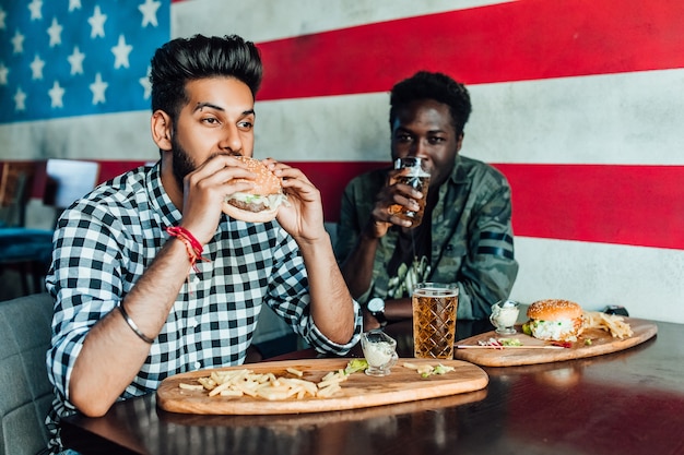 Dos hombres negros hambrientos divirtiéndose mientras pasan tiempo con amigos en un pub y beben cerveza.