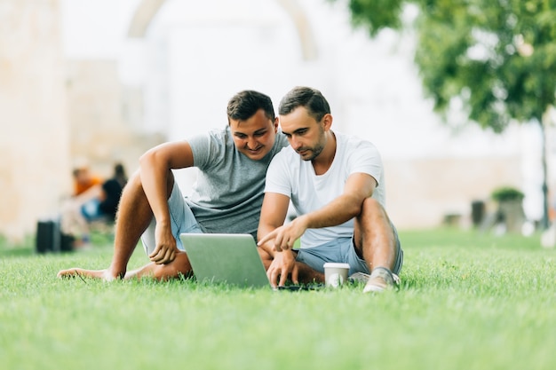 Dos hombres que trabajan con el portátil en verde en el parque