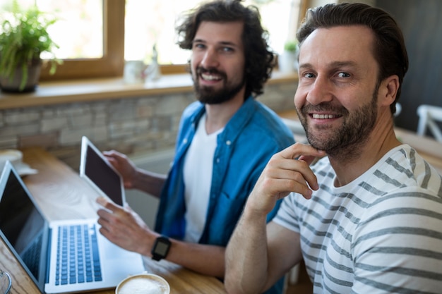 Dos hombres que usan la tableta digital y un ordenador portátil en una cafetería