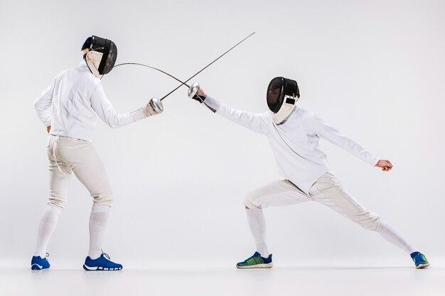 Los dos hombres con traje de esgrima practicando con espada contra gris