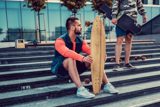 Dos hombres urbanos posando con longboard en escalones en el centro.