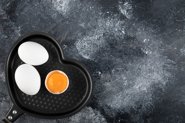 Dos huevos blancos y yema en sartén en forma de corazón.