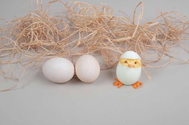 Dos huevos de gallina blancos frescos con juguete de gallina y heno.