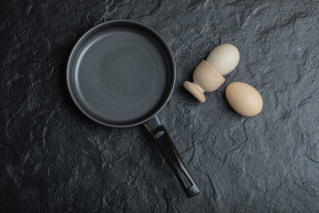 Dos huevos y una sartén negra sobre fondo negro.