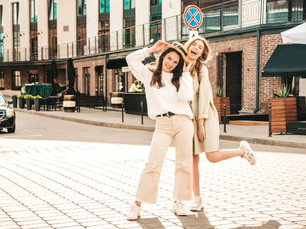 Dos joven hermosa mujer sonriente hipster en abrigo y suéter blanco de moda