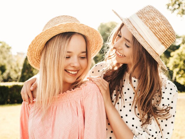 Dos joven hermosa mujer sonriente hipster en vestido de verano de moda. Mujeres despreocupadas sexy posando en el parque con sombreros.