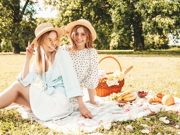 Dos joven hermosa mujer sonriente hipster en vestido de verano y sombreros. Mujeres despreocupadas haciendo picnic afuera.