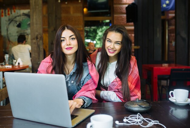 Dos joven y hermosa niña sentada en la mesa y buscando algo en Internet