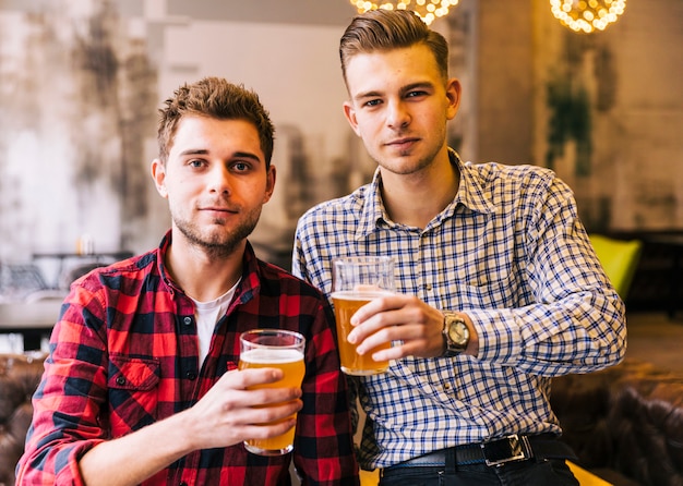 Dos joven sosteniendo los vasos de cerveza en pub