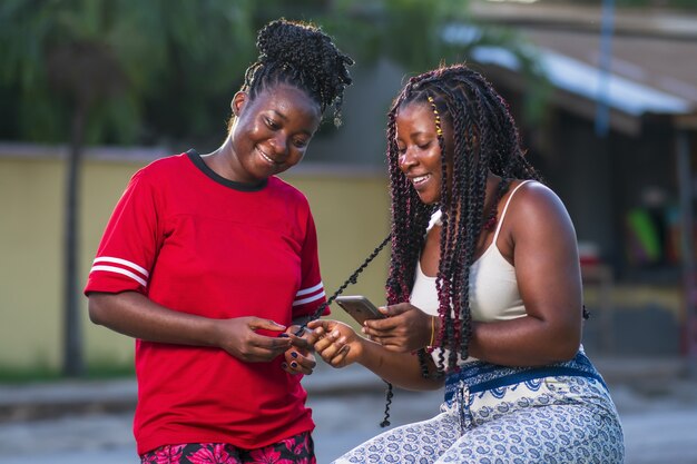 Dos jóvenes amigas afroamericanas mirando un teléfono y sonriendo