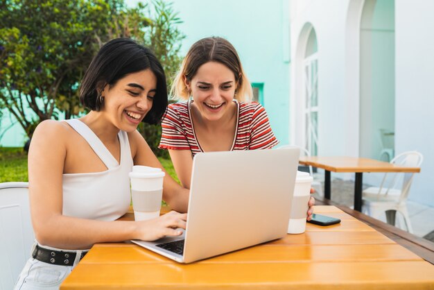 Dos jóvenes amigos usando una computadora portátil en la cafetería.