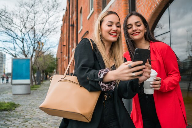 Dos jóvenes amigos usando su teléfono móvil al aire libre.