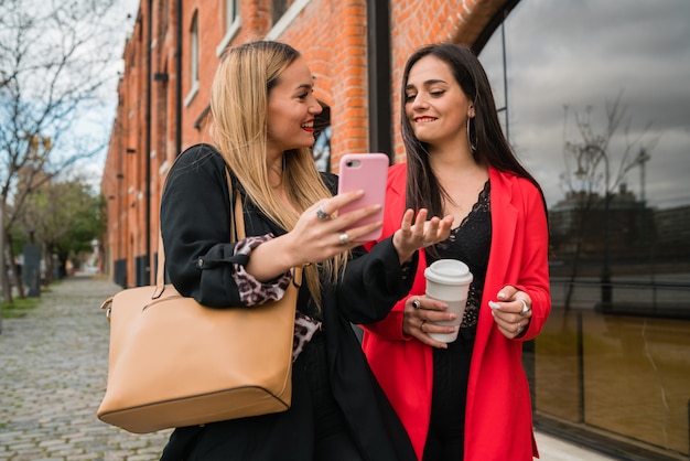 Dos jóvenes amigos usando su teléfono móvil al aire libre.