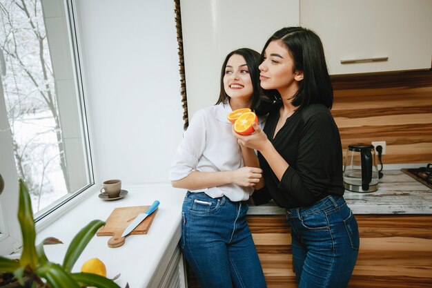 dos jóvenes y bonita morena de pie junto a la ventana en la cocina con naranja