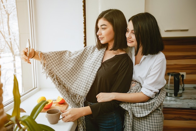 dos jóvenes y bonita morena de pie junto a la ventana en la cocina con naranja