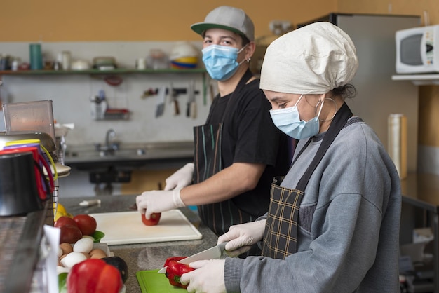 Dos jóvenes chefs cortando verduras con máscaras médicas