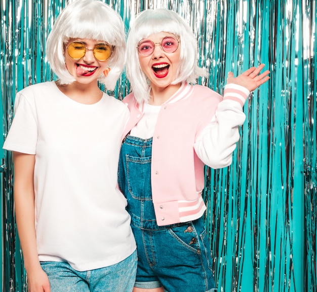 Dos jóvenes chicas sexy hipster con pelucas blancas y labios rojos. Hermosas mujeres de moda en ropa de verano con gafas de sol de verano