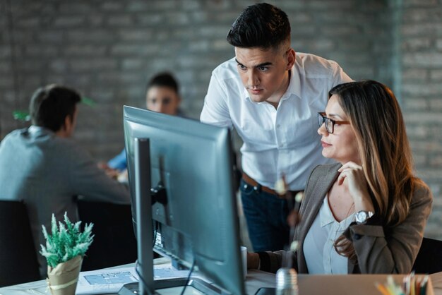 Dos jóvenes colegas de negocios que usan PC de escritorio y leen un correo electrónico mientras trabajan juntos en la oficina El foco está en el hombre