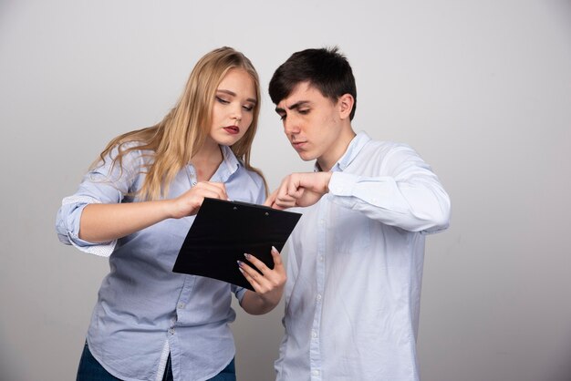 Dos jóvenes colegas de oficina discutiendo un proyecto en la pared gris.