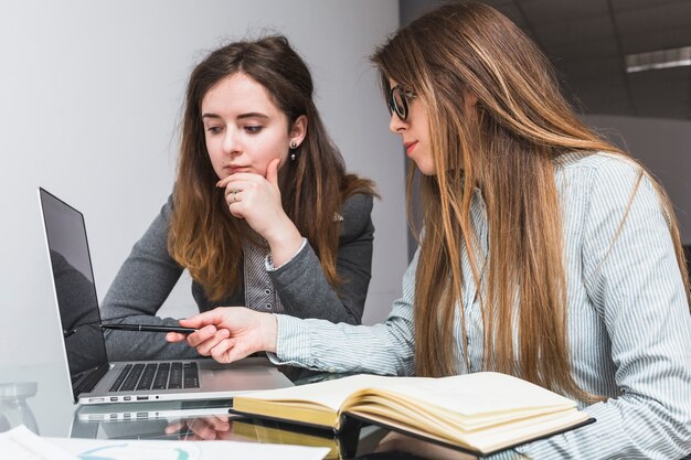 Dos jóvenes empresarias usando la computadora portátil en la oficina