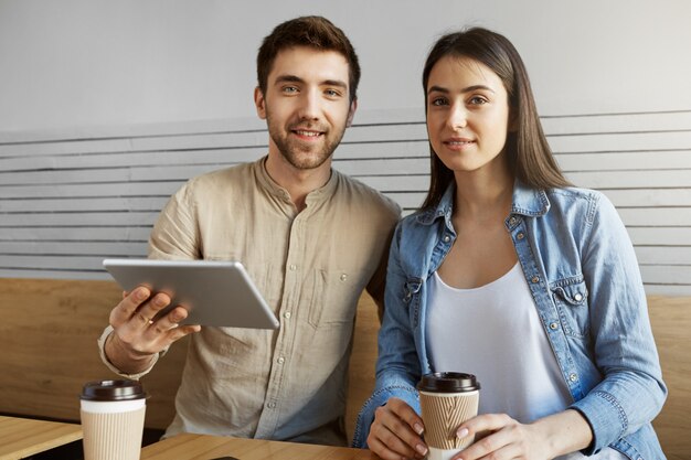 Dos jóvenes empresarios ambiciosos en reunión en la cafetería hablando sobre el plan de negocios en el mes siguiente calculando estadísticas con tableta digital. Trabajo en equipo, concepto de negocio