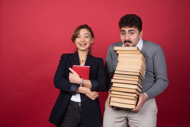 Dos jóvenes empresarios con libros de pie sobre la pared roja