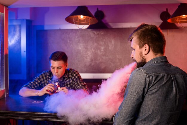 Dos jóvenes fuman cigarrillos electrónicos en un vapebar. tienda de vapeo